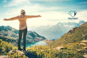 Traveling for rehab concept pic shows a woman atop a mountain with outstretched arms